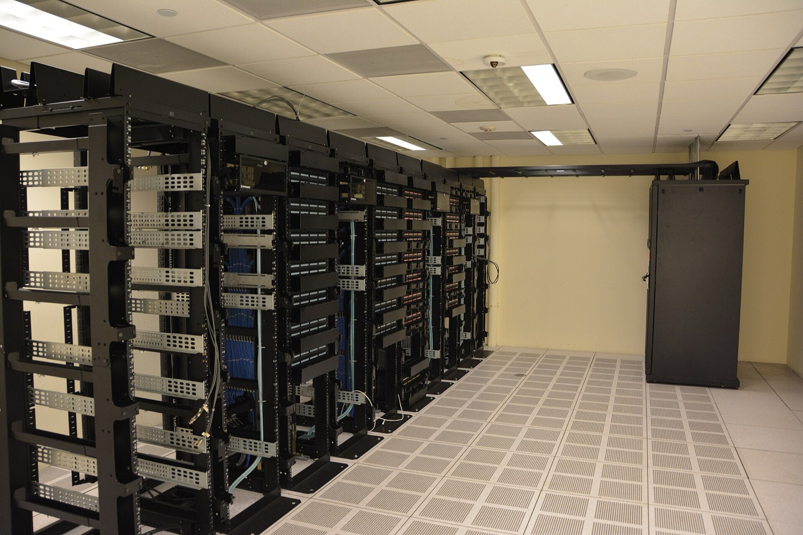 Rows of open server racks on a raised floor in a data hall, with an in-row cooling unit at the end