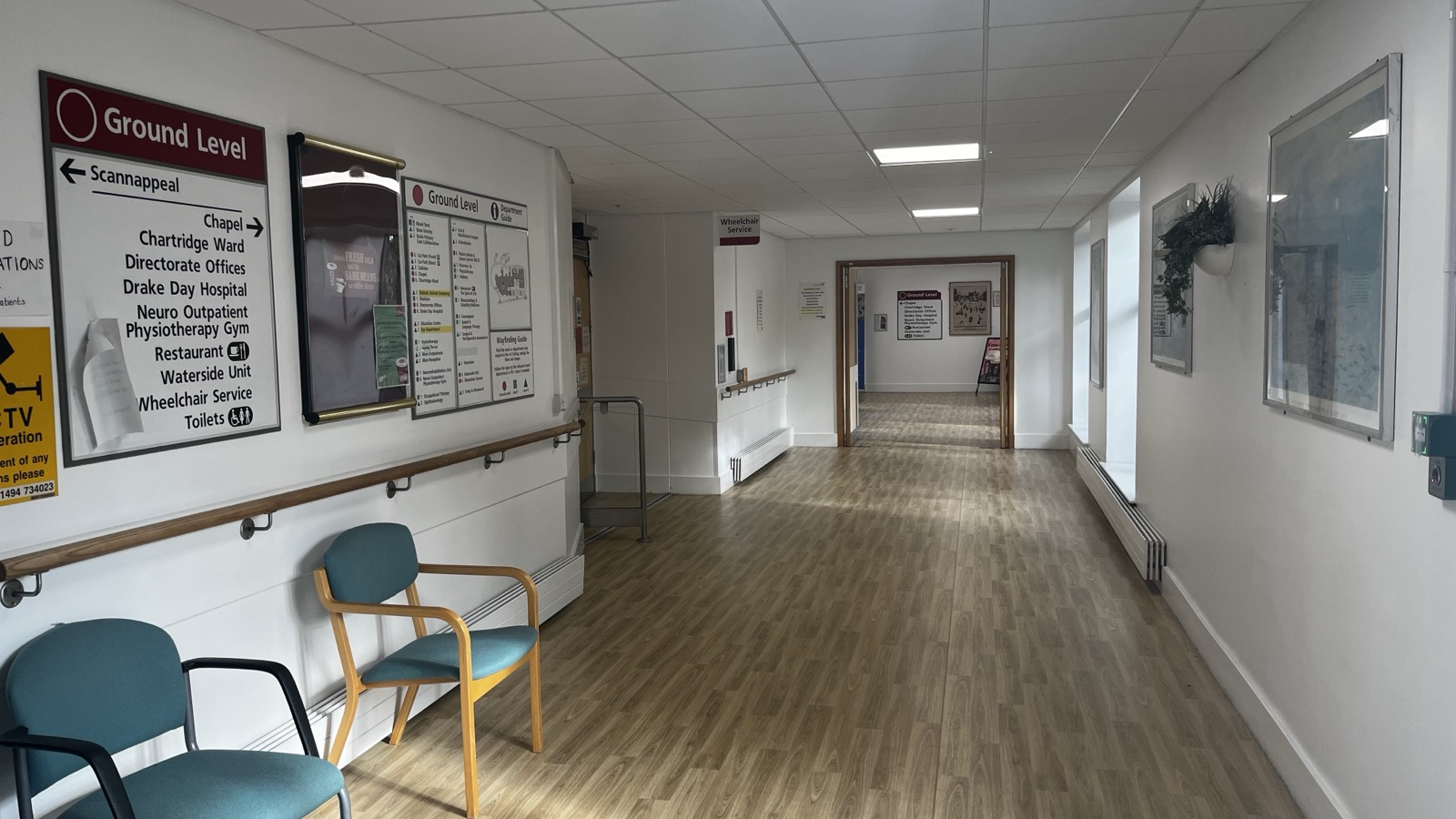 Empty hospital corridor with wayfinding signs, handrail and chairs leading to a set of doors