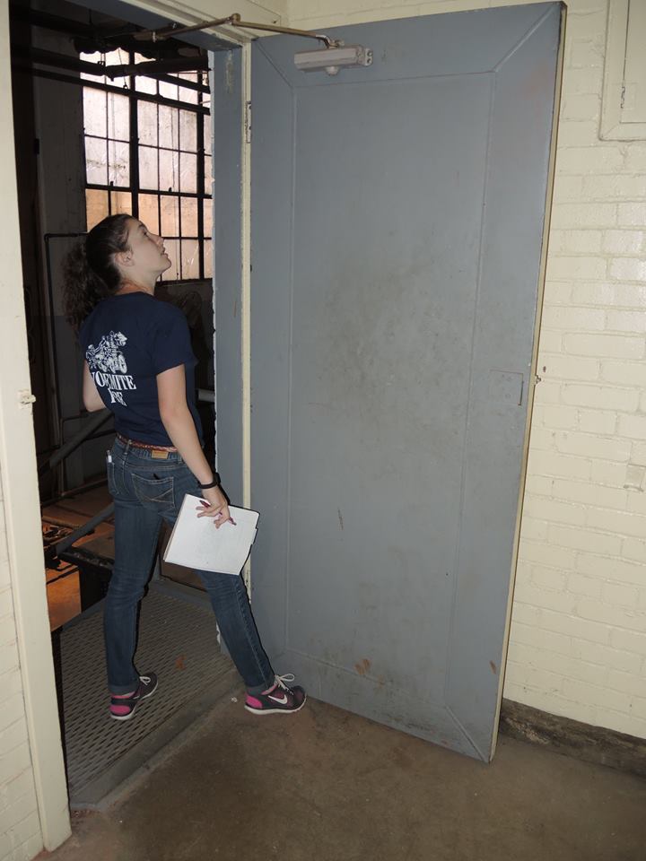 Inspector looking up at the top edge and closer of a steel fire door during a fire safety inspection