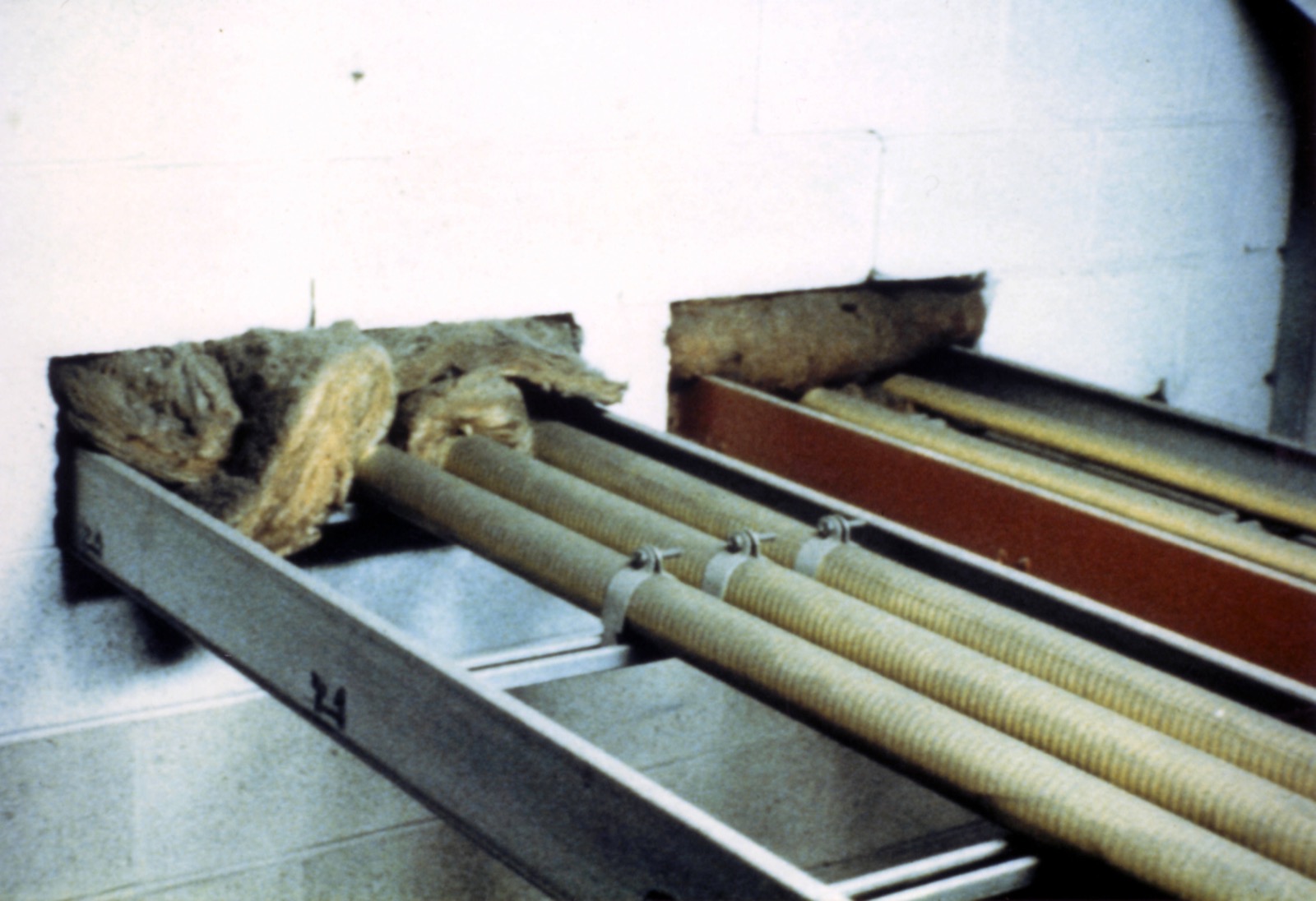 Cable tray passing through a wall opening packed with loose insulation batts, an example of an inadequate fire stopping detail